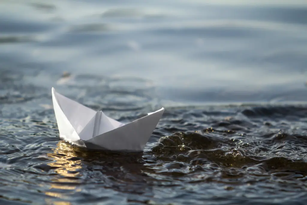 close small white origami paper boat floating on water