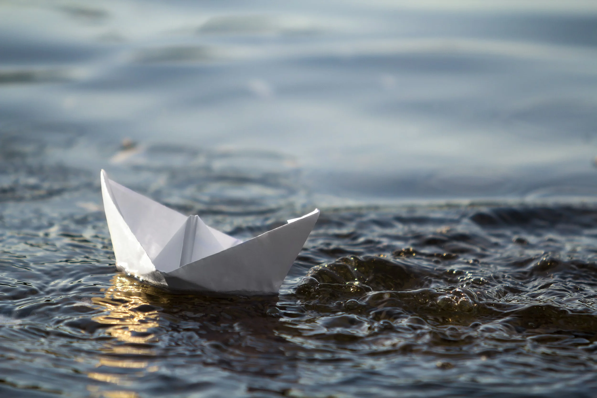 close small white origami paper boat floating on water